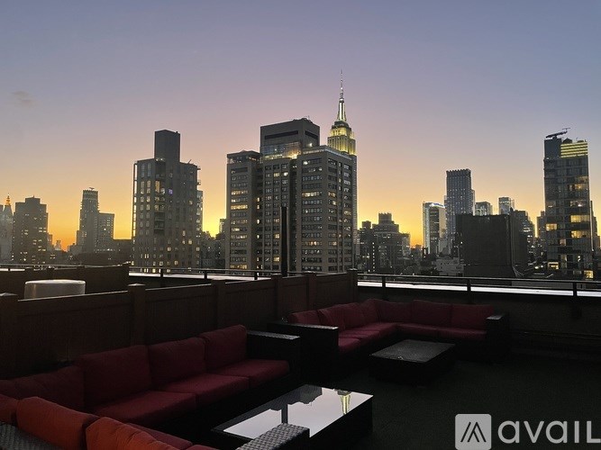 A red couch is on a balcony overlooking a city skyline at dusk.