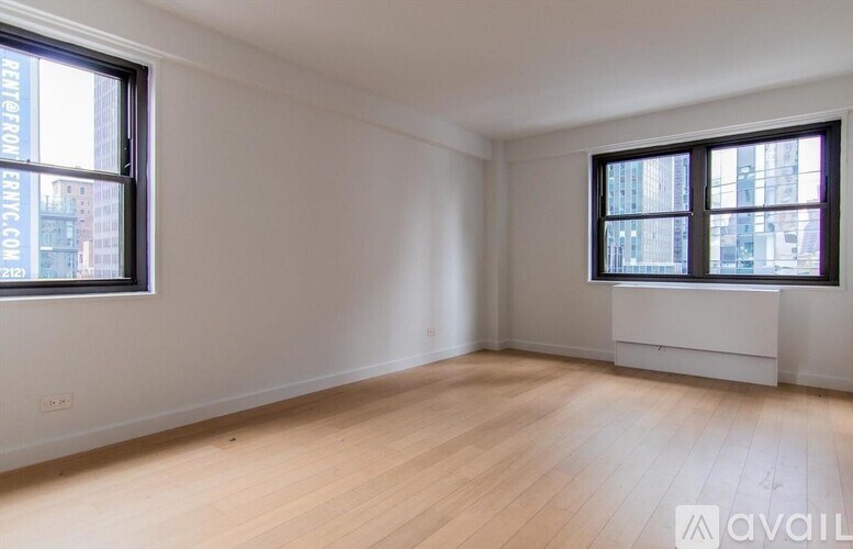 A room with wooden flooring and two windows.
