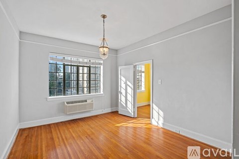 A room with wooden floors and white walls, featuring a window with blinds and a yellow door.