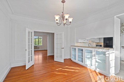A chandelier hangs over a kitchen island with a sink and a refrigerator.