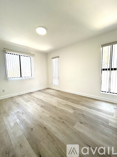 A room with wooden flooring and two windows.