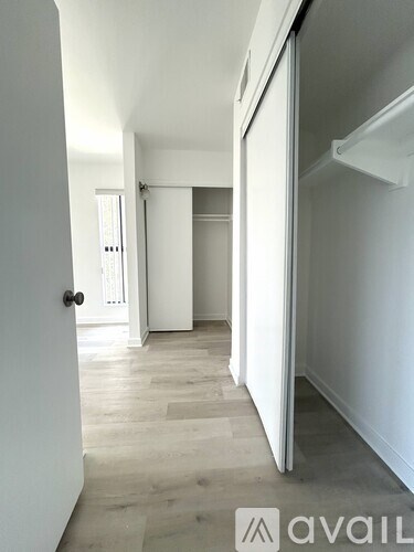 A hallway with a door on the left and a refrigerator on the right.