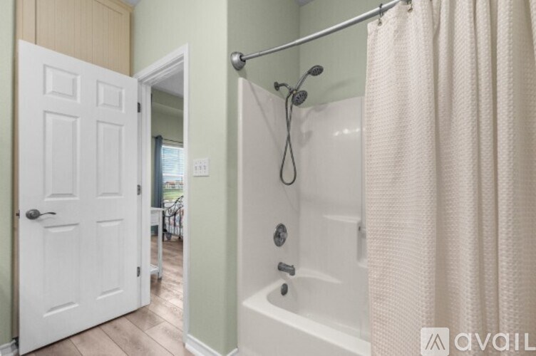 A white door is open to a bathroom with a white tub and a white shower curtain.