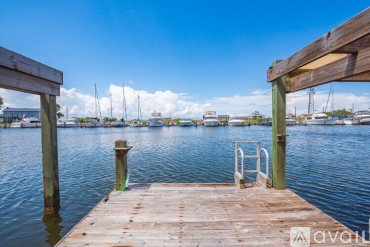 A wooden dock extends into a calm body of water with boats docked in the distance.