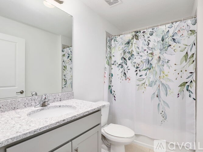 A bathroom with a floral shower curtain and a white toilet.