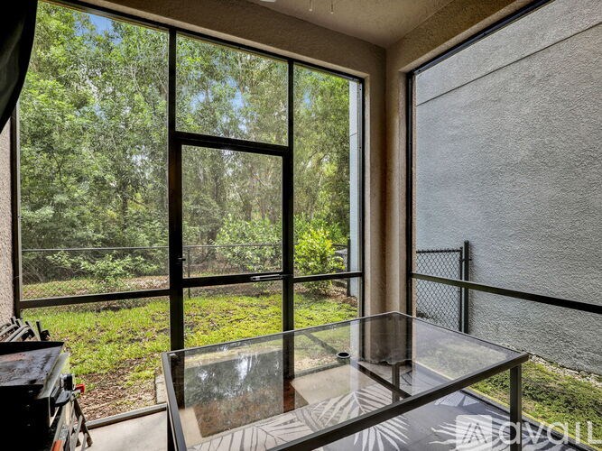 A glass table is in a room with a view of the trees outside.