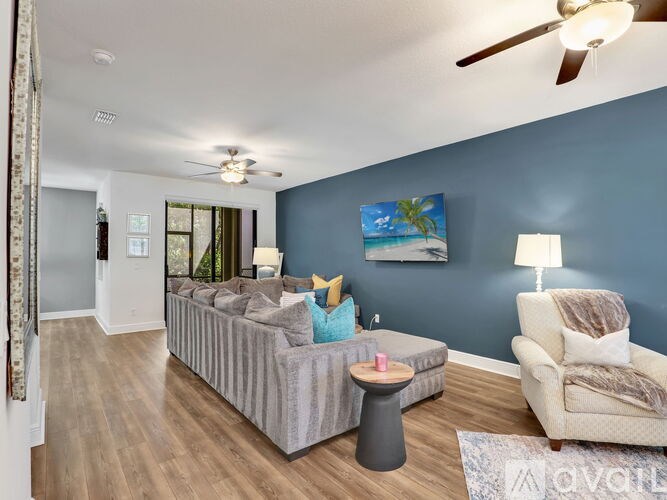 A living room with a grey couch, a white armchair, and a painting of a beach scene on the wall.