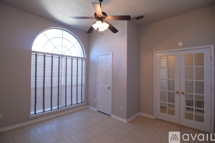 A room with a ceiling fan and a large window with blinds.