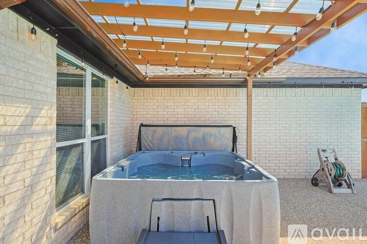 A hot tub is on a patio with a bed and a hose reel.