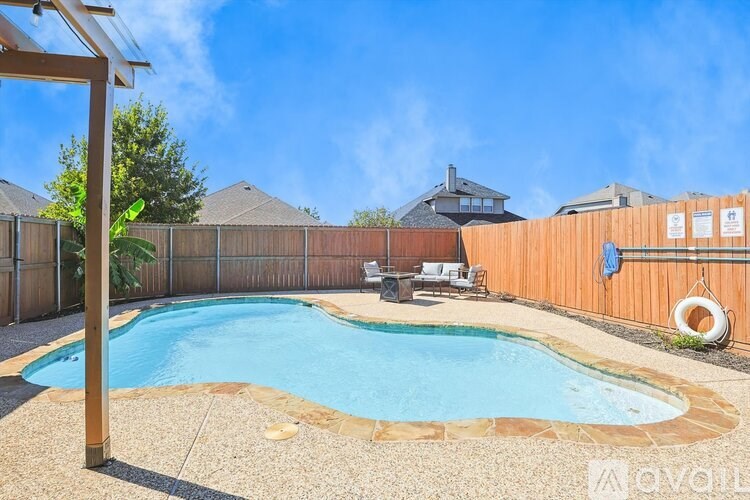 A pool surrounded by a wooden fence and a patio area with chairs and a table.