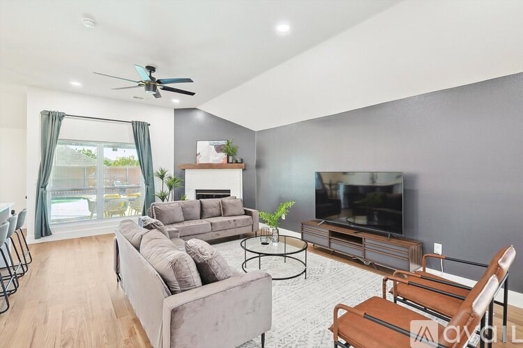 A living room with a grey couch, a black chair, a small table, a television, and a fireplace.