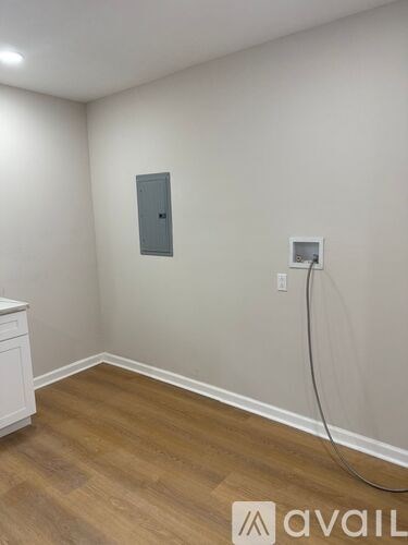 A room with a wooden floor and a white wall with a grey door and a white electrical outlet.