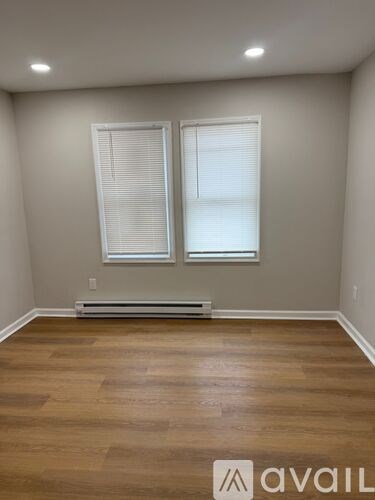 A room with wooden flooring and two windows.
