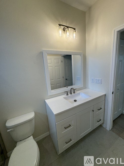 A white bathroom with a toilet, sink, and mirror.