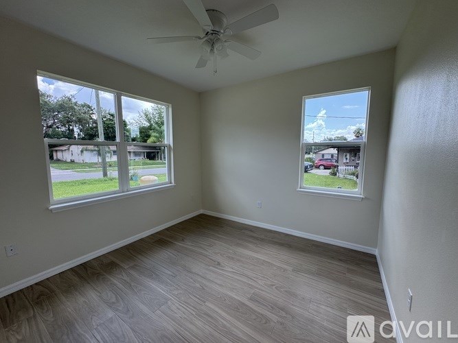 A room with a ceiling fan and two windows overlooking a street.