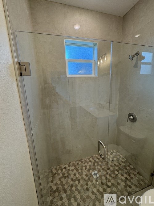 A bathroom with a glass shower stall and a window.
