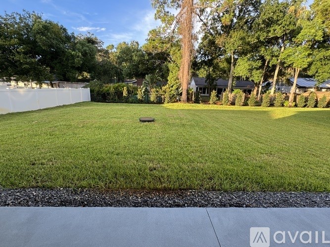 A well-maintained lawn with a white fence and trees in the background.