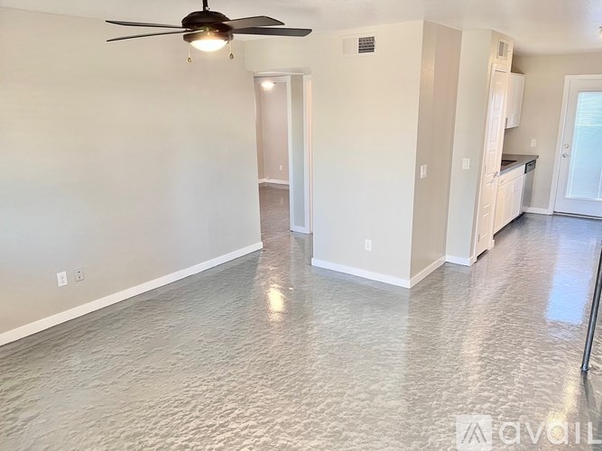 A spacious room with a ceiling fan and a kitchen area in the background.