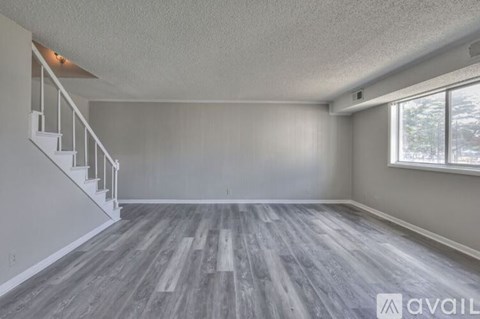 A spacious room with wooden flooring and a staircase.