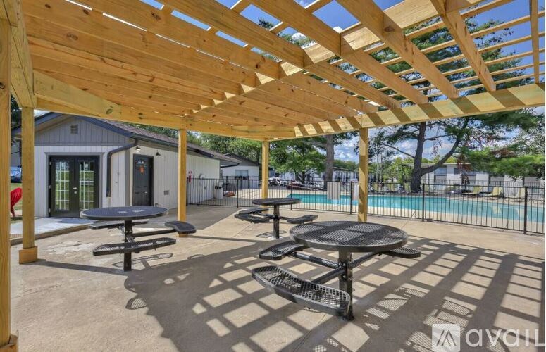 A wooden pergola over a patio with tables and a pool in the background.