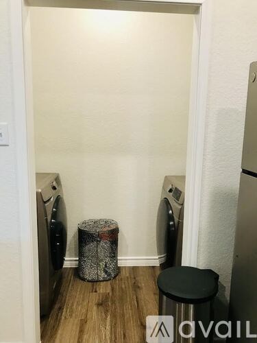 A small room with a washing machine and a trash can.