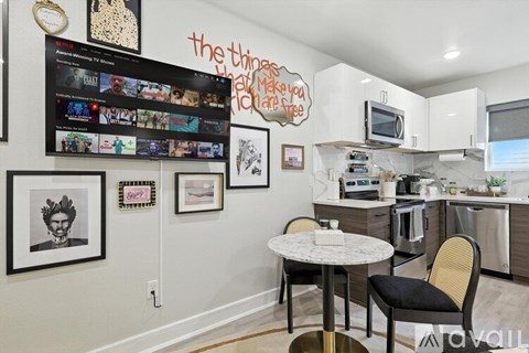 A kitchen with a table and chairs in front of a wall with pictures and a TV.