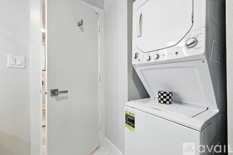 A white washing machine is in a small room with a door on the left.