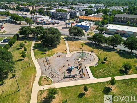 A playground with a slide, swings, and a seesaw is surrounded by trees and grass.