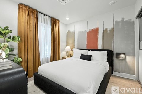 A bedroom with a large bed, a plant, and a wall with a cityscape painting.