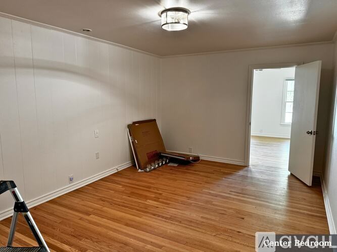 A room with wooden floors and a white wall with a doorway leading to another room.