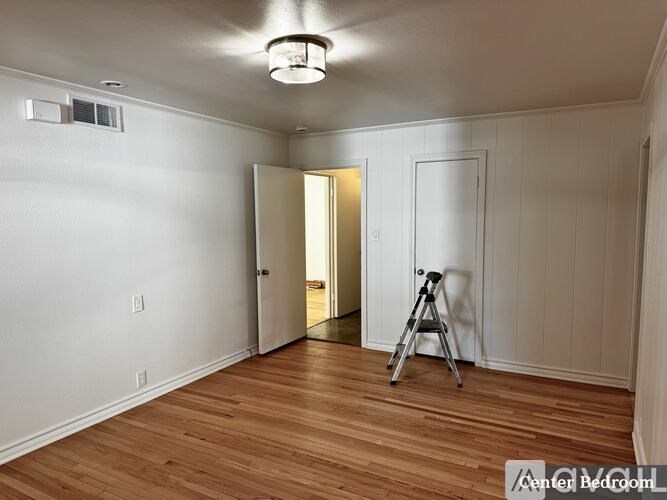 A room with wooden floors and white walls, with a tripod in the middle of the room.