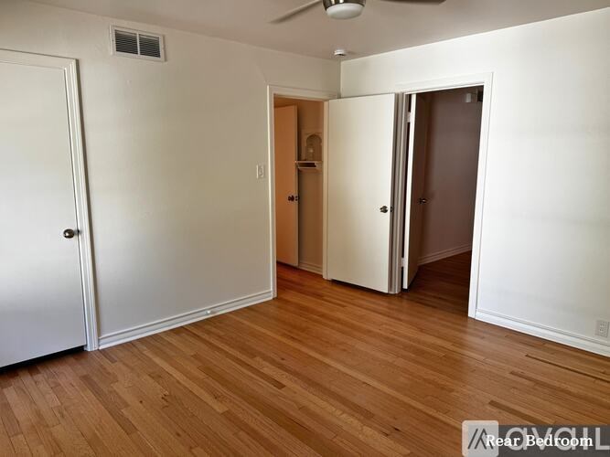 A room with a white door, a brown door, and a white wall with a fan.