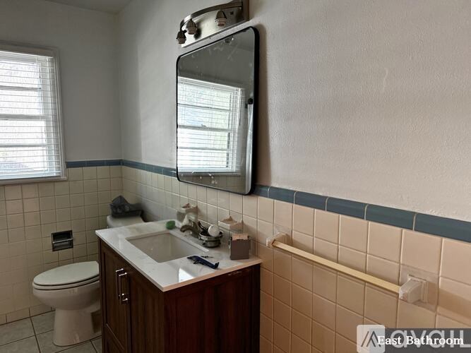 A bathroom with a toilet, sink, mirror and tiled walls.