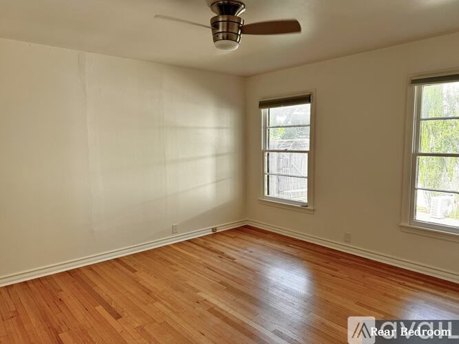 A room with a ceiling fan and two windows.