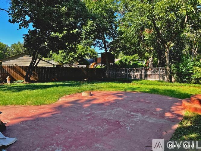 A backyard with a red concrete area and a wooden fence.