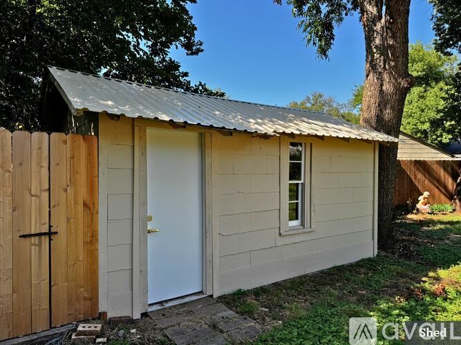 A shed with a metal roof and a white door is surrounded by a wooden fence.