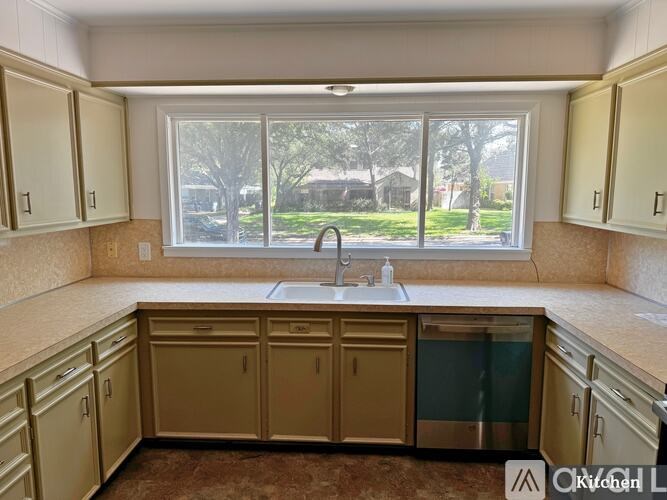 A kitchen with beige cabinets and a window overlooking a green area.