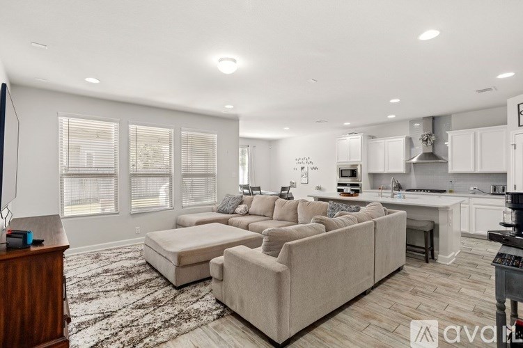 A modern living room with a large beige sofa and a kitchen area in the background.