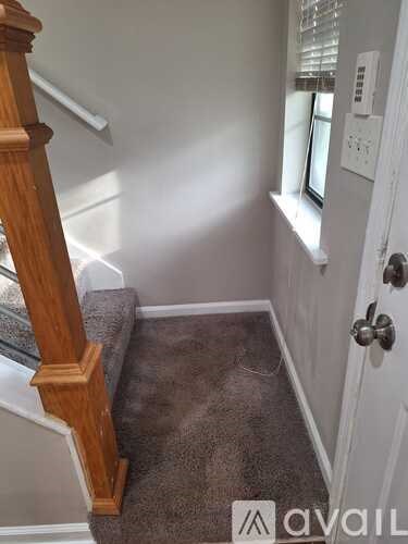 A room with a carpeted floor, a wooden staircase, and a door with a handle.