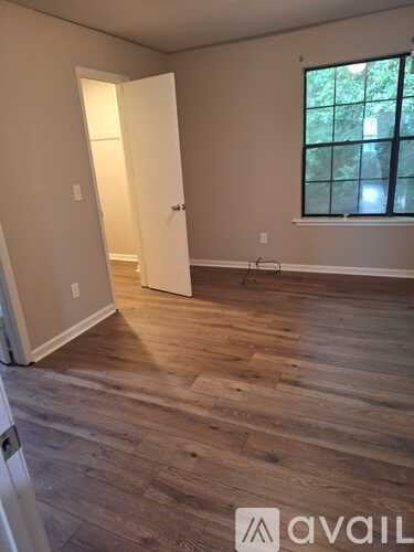 A room with wooden flooring and a window with a view of trees outside.