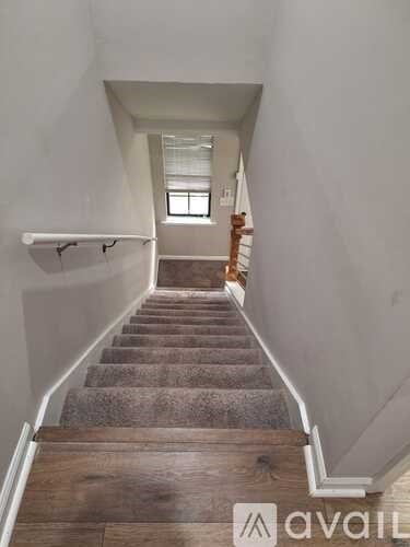A staircase with wooden steps and a carpeted runner leads up to a bright window.