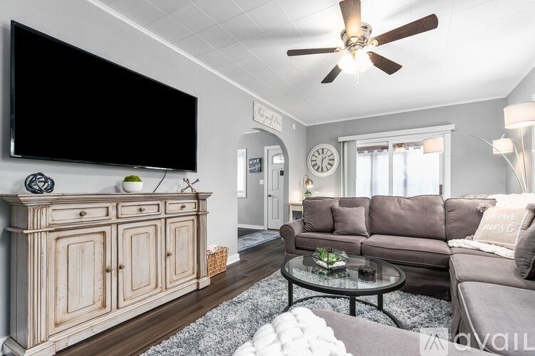 A living room with a grey sofa, a wooden cabinet, and a black TV mounted on the wall.