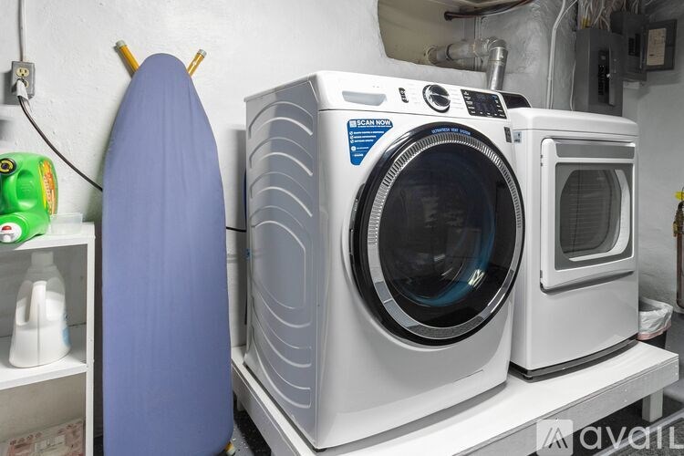 A large industrial washing machine sits in a room with a blue surfboard leaning against it.