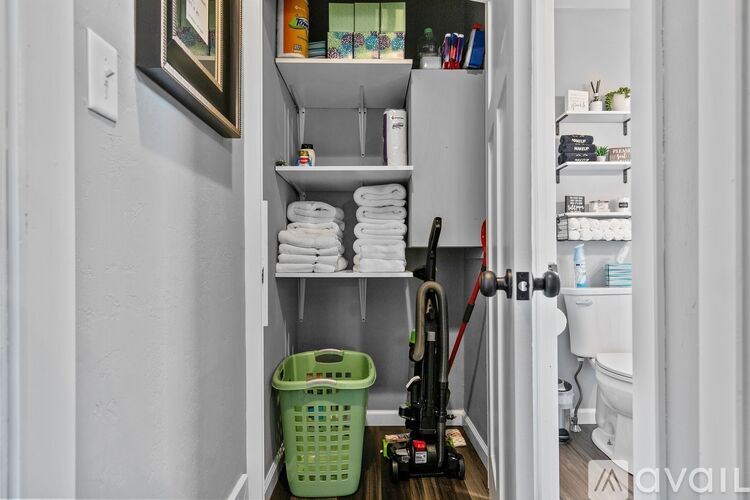 A bathroom with a vacuum cleaner and towels on the shelves.