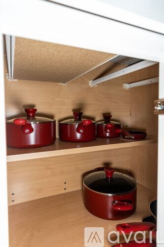A kitchen cabinet with three red pots on the shelf.