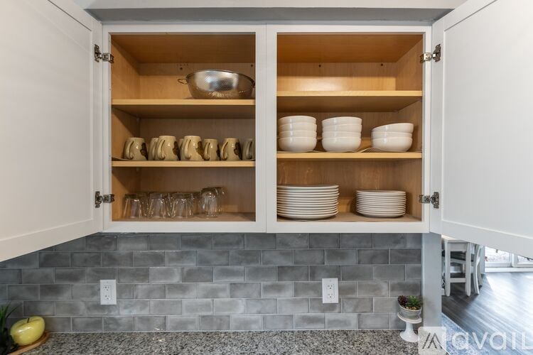 A kitchen cabinet with glass doors is open, revealing plates and bowls inside.