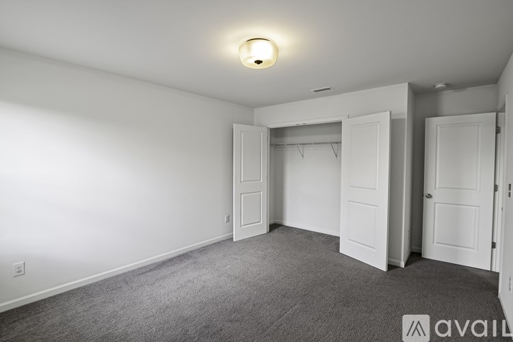 A room with a carpeted floor and white walls, featuring a single light fixture and three closet doors.