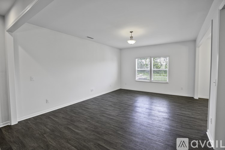 A spacious room with wooden flooring and a window with blinds.