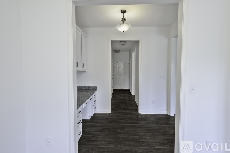 A long hallway with a light on the ceiling and a kitchen area on the left.