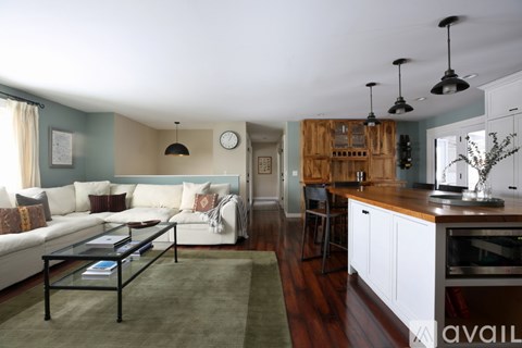 A modern living room with a glass coffee table and a kitchen area in the background.